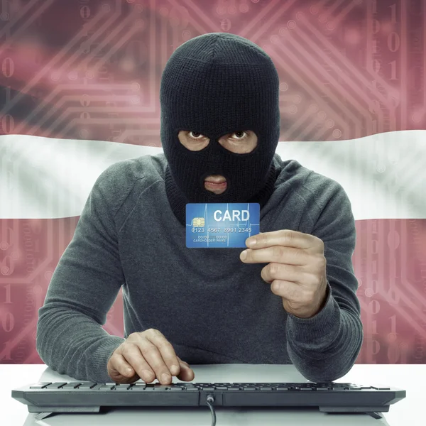 Dark-skinned hacker with flag on background holding credit card in hand - Latvia —  Fotos de Stock