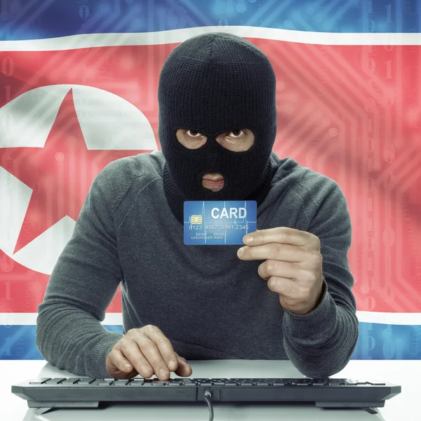 Dark-skinned hacker with flag on background holding credit card in hand - North Korea — 图库照片