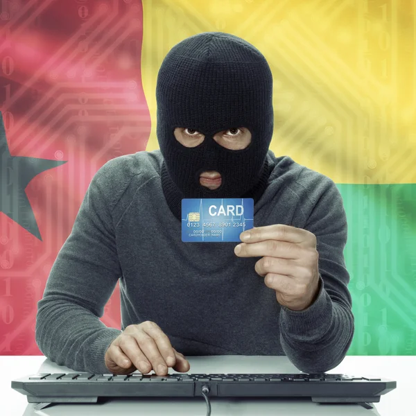 Dark-skinned hacker with flag on background holding credit card in hand - Guinea-Bissau — Zdjęcie stockowe