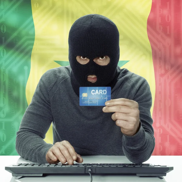 Dark-skinned hacker with flag on background holding credit card in hand - Senegal — Zdjęcie stockowe