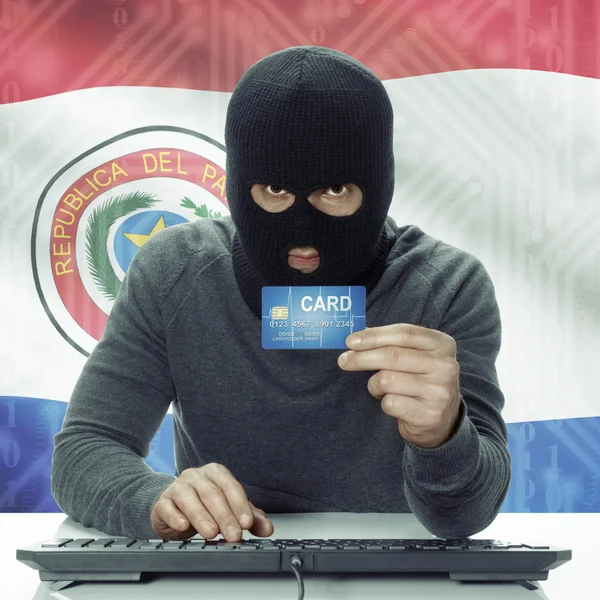 Dark-skinned hacker with flag on background holding credit card in hand - Paraguay — стокове фото