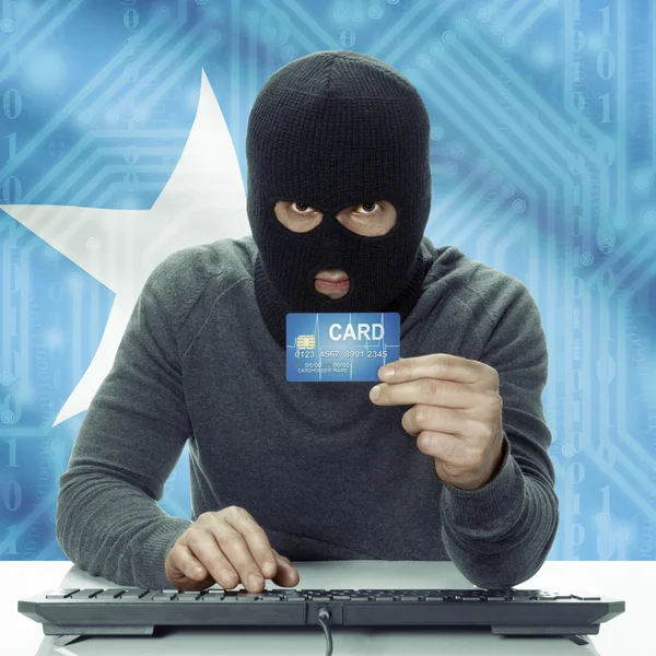 Dark-skinned hacker with flag on background holding credit card in hand - Somalia — Stok fotoğraf