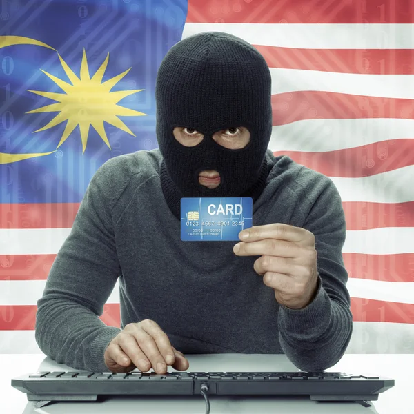 Dark-skinned hacker with flag on background holding credit card in hand - Malaysia — Stock Photo, Image