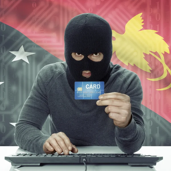 Dark-skinned hacker with flag on background holding credit card in hand - Papua New Guinea - Stock-foto