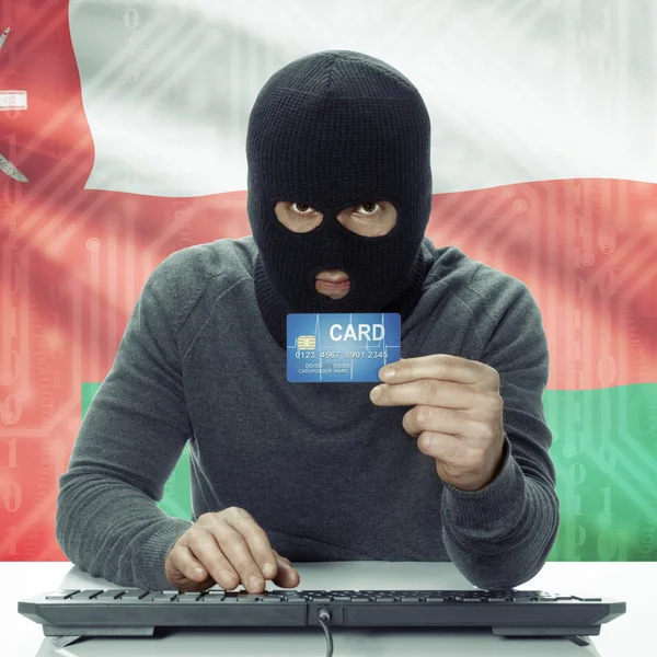 Dark-skinned hacker with flag on background holding credit card in hand - Oman — Stock Photo, Image