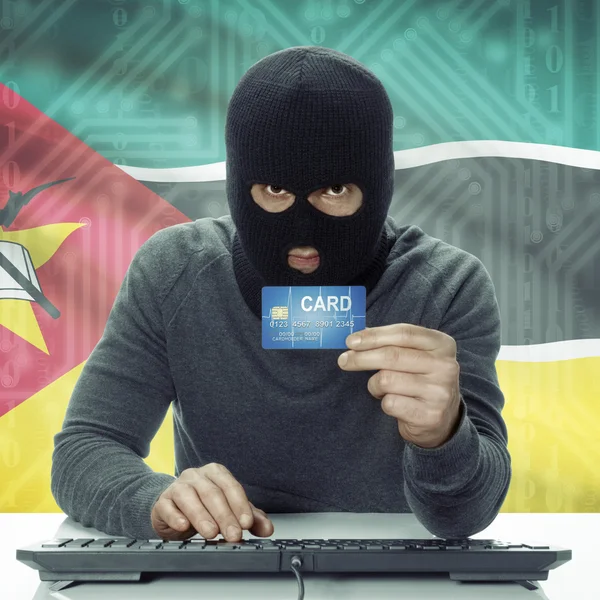 Dark-skinned hacker with flag on background holding credit card in hand - Mozambique — Stock Photo, Image