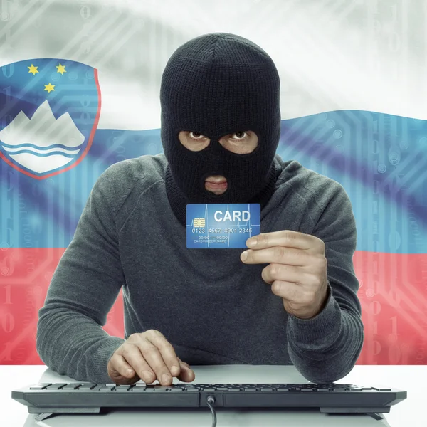 Dark-skinned hacker with flag on background holding credit card in hand - Slovenia — Stock Photo, Image