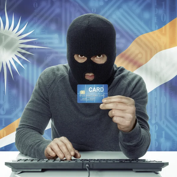 Dark-skinned hacker with flag on background holding credit card in hand - Marshall Islands — Stock Photo, Image