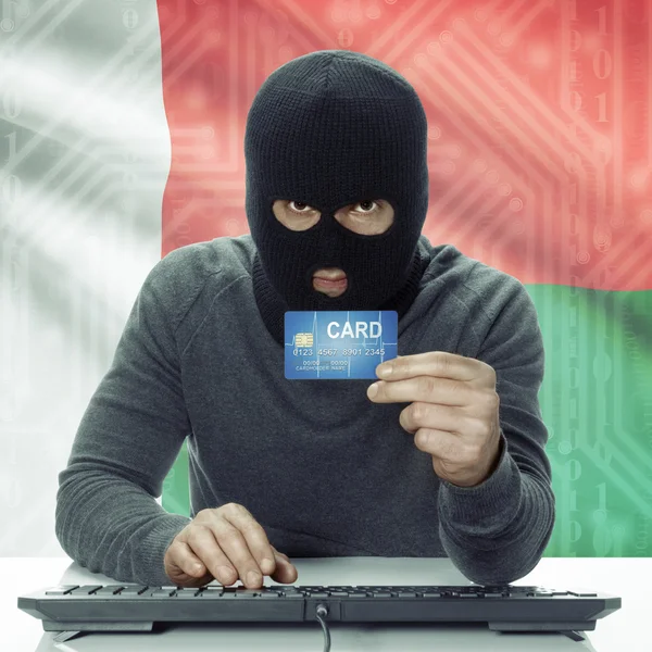 Dark-skinned hacker with flag on background holding credit card in hand - Madagascar — Stock Photo, Image