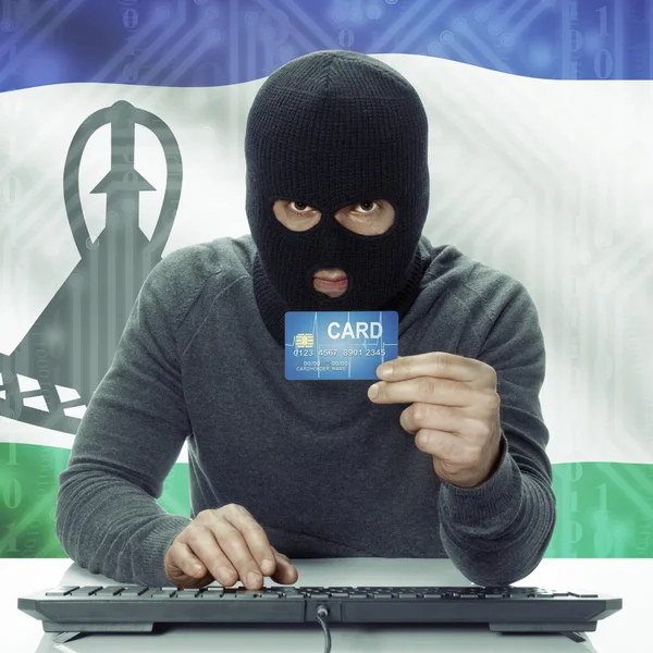 Dark-skinned hacker with flag on background holding credit card in hand - Lesotho — Stock Photo, Image