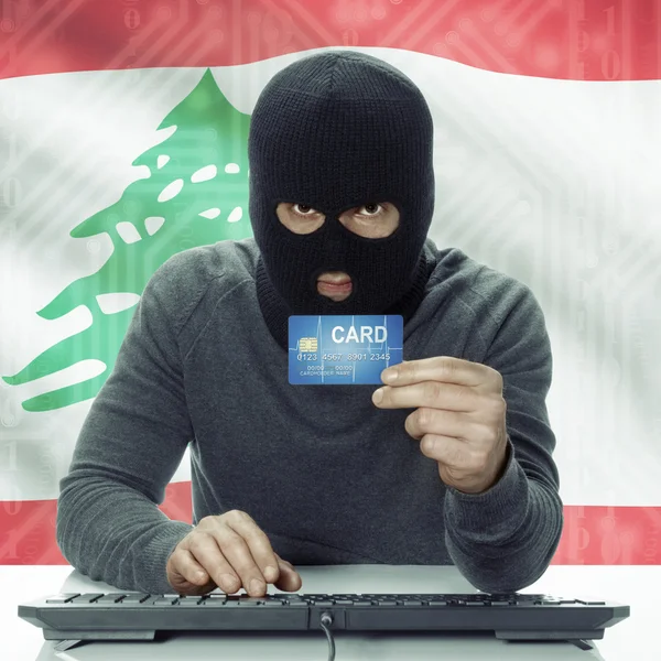 Dark-skinned hacker with flag on background holding credit card in hand - Lebanon — Stock Photo, Image