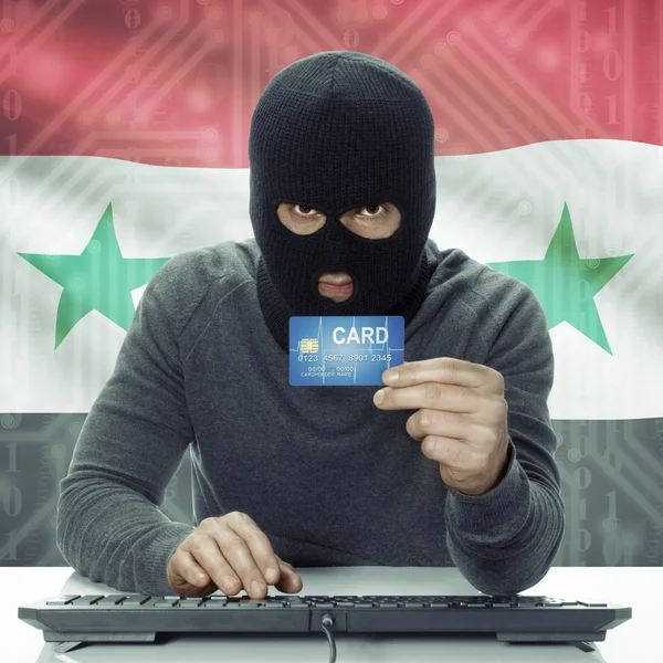 Dark-skinned hacker with flag on background holding credit card in hand - Syria — Stock Photo, Image