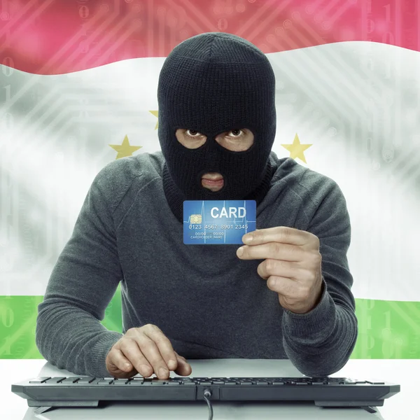 Dark-skinned hacker with flag on background holding credit card in hand - Tajikistan — Stock Photo, Image