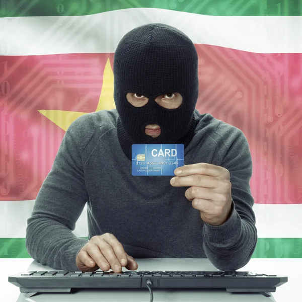 Dark-skinned hacker with flag on background holding credit card in hand - Suriname — Stock Photo, Image