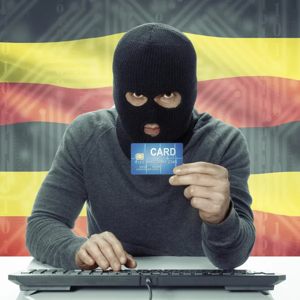 Dark-skinned hacker with flag on background holding credit card in hand - Uganda — Stock fotografie