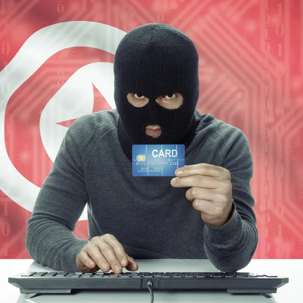 Dark-skinned hacker with flag on background holding credit card in hand - Tunisia — Stock Photo, Image