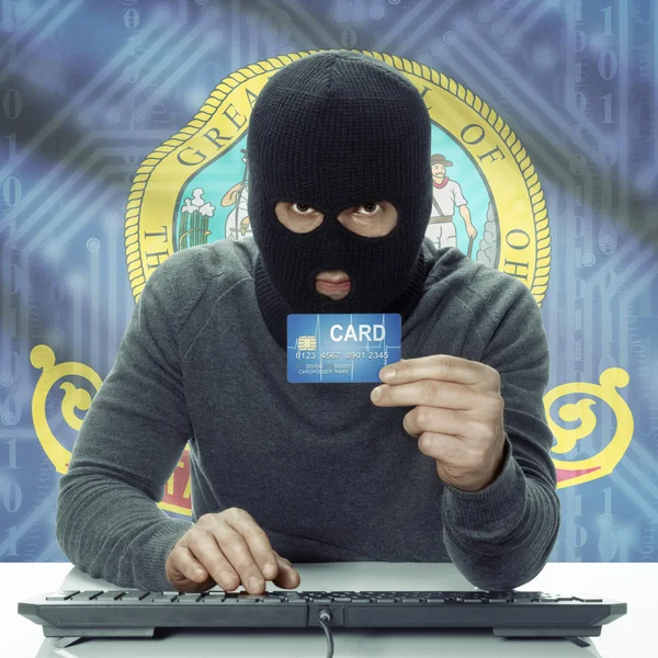 Dark-skinned hacker with USA states flag on background holding card in hand - Idaho — Stock fotografie