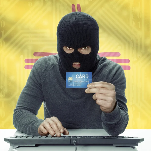 Dark-skinned hacker with USA states flag on background holding card in hand - New Mexico — стокове фото