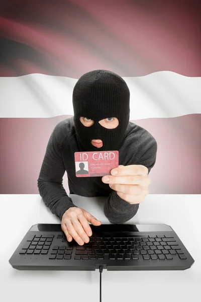 Arka planda bayrağı olan bir hacker kimlik kartını elinde tutuyor - Letonya — Stok fotoğraf