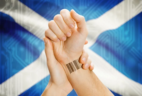 Barcode ID number on wrist and national flag on background - Scotland — Stock Photo, Image