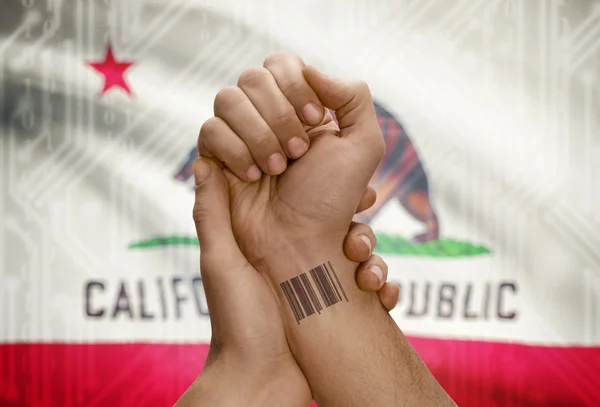 Barcode ID number on wrist of dark skinned person and USA states flags on background - California — Foto Stock