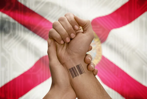 Barcode ID number on wrist of dark skinned person and USA states flags on background - Florida —  Fotos de Stock