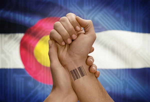 Barcode ID number on wrist of dark skinned person and USA states flags on background - Colorado — Stockfoto