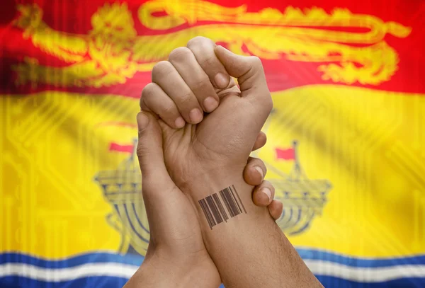 Barcode ID number on wrist of dark skin person and Canadian province flag on background - New Brunswick — 图库照片