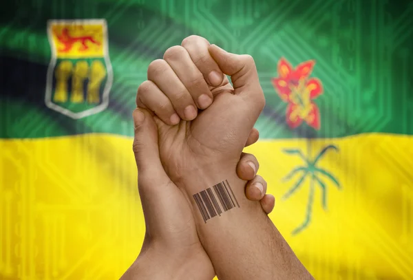 Barcode ID number on wrist of dark skin person and Canadian province flag on background - Saskatchewan — Stok fotoğraf