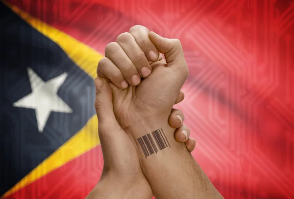 Barcode ID number on wrist of dark skinned person and national flag on background - East Timor — Stock Photo, Image