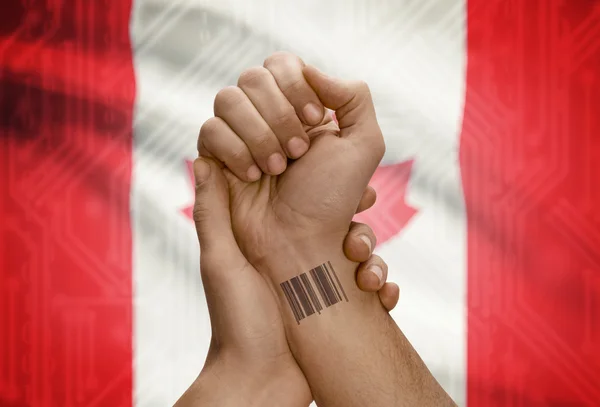 Barcode ID number on wrist of dark skinned person and national flag on background - Canada — 图库照片