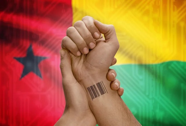 Barcode ID number on wrist of dark skinned person and national flag on background - Guinea-Bissau — Stock Photo, Image