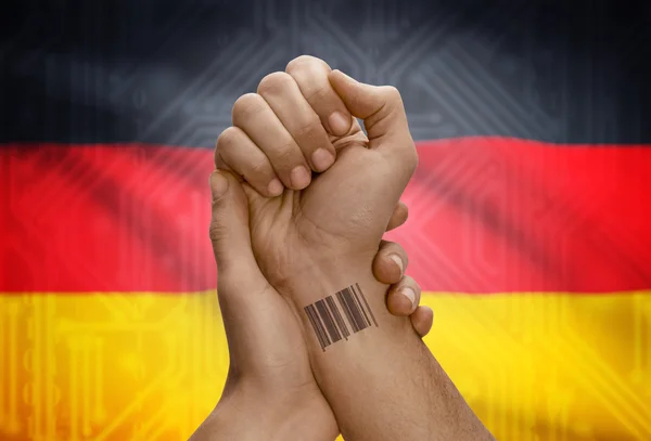 Barcode ID number on wrist of dark skinned person and national flag on background - Germany — kuvapankkivalokuva