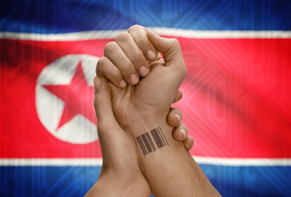 Barcode ID number on wrist of dark skinned person and national flag on background - North Korea — Zdjęcie stockowe
