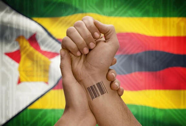 Barcode ID number on wrist of dark skinned person and national flag on background - Zimbabwe — 图库照片