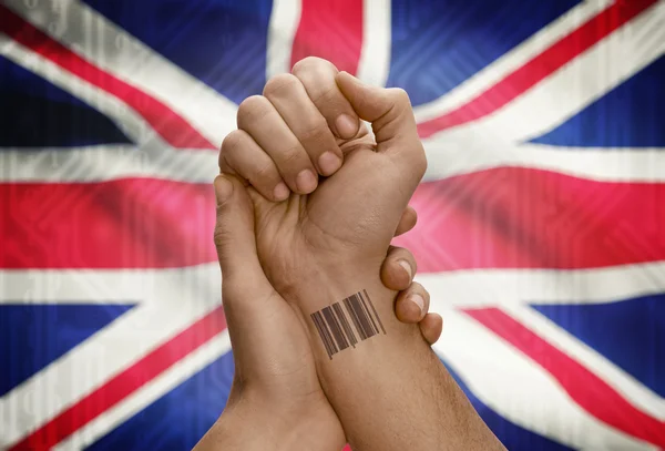 Barcode ID number on wrist of dark skinned person and national flag on background - United Kingdom — Stock Photo, Image