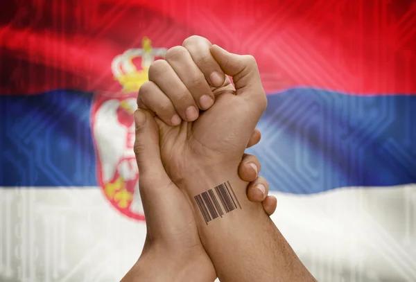 Barcode ID number on wrist of dark skinned person and national flag on background - Serbia — Stock Photo, Image
