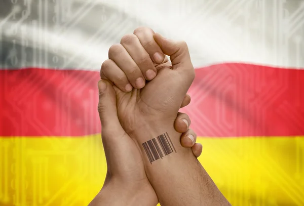 Barcode ID number on wrist of dark skinned person and national flag on background - South Ossetia — kuvapankkivalokuva