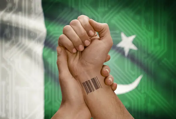 Barcode ID number on wrist of dark skinned person and national flag on background - Pakistan — Stock fotografie