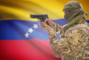 Male in muslim keffiyeh with gun in hand and national flag on background - Venezuela