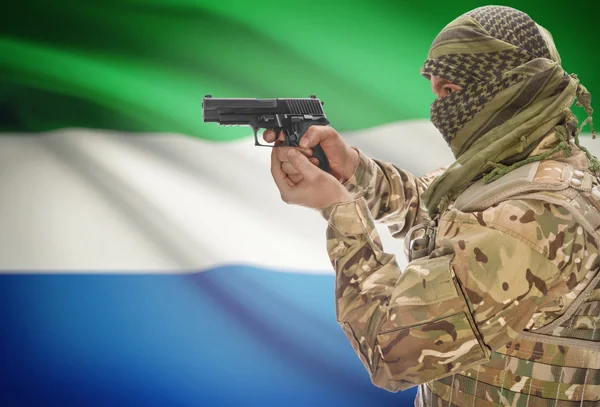 Male in muslim keffiyeh with gun in hand and national flag on background - Sierra Leone — стокове фото
