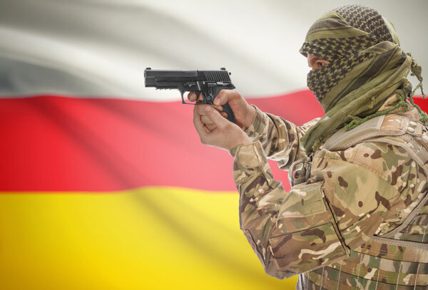 Male in muslim keffiyeh with gun in hand and national flag on background - South Ossetia