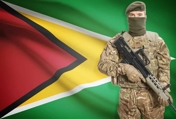 Soldier holding machine gun with flag on background series - Guyana — Stock fotografie