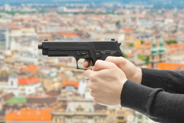 Man med en pistol redo att skjuta - fokusera på pistol och suddiga landskapet i staden på bakgrund — Stockfoto