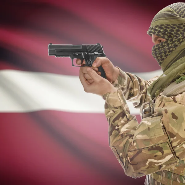 ชายที่มีปืนอยู่ในมือและธงชาติบนพื้นหลัง ลัตเวีย — ภาพถ่ายสต็อก