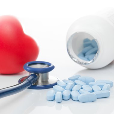 Stetoskop, bir şişe hap ve masada kırmızı kalp, yakın çekim