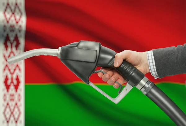 Bocal da bomba de combustível na mão com a bandeira nacional no plano de fundo - Bielorrússia — Fotografia de Stock