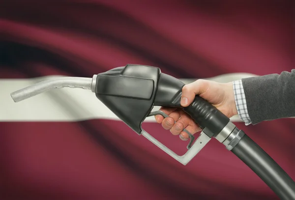 Bocal da bomba de combustível na mão com a bandeira nacional no plano de fundo - Letónia — Fotografia de Stock