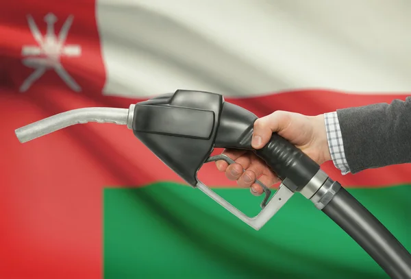 Fuel pump nozzle in hand with national flag on background - Oman