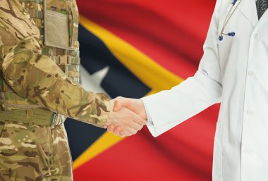 Military man in uniform and doctor shaking hands with national flag on background - East Timor
